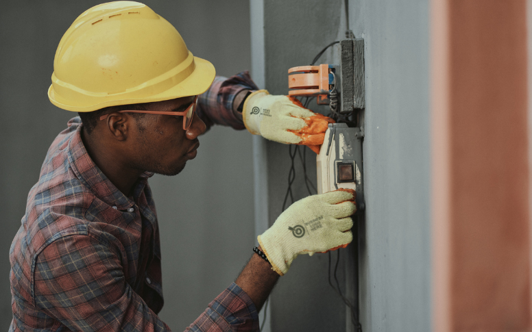 An electrician wearing a yellow hard and electrician gloves with company logo on it